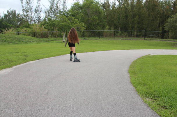 Jonge vrouw rolschaatsen buiten in het park - Foto, afbeelding