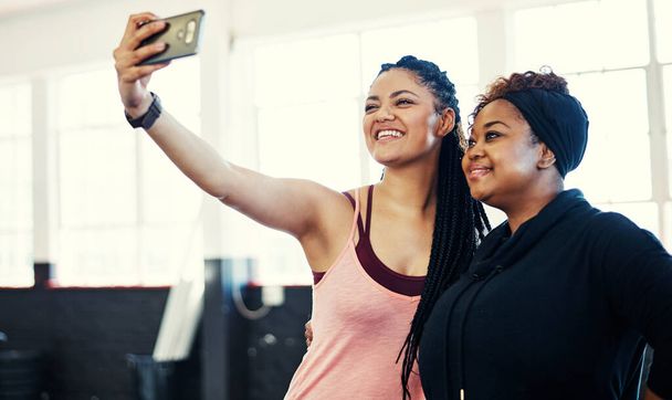 Fitness faces. two cheerful young women taking a self portrait together before a workout session in a gym - Fotografie, Obrázek