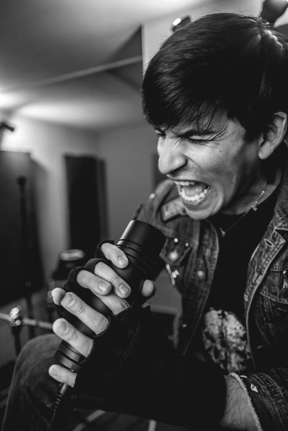 Passionate and intense young rocker vocalist unleashing raw energy during intense metal performance in a rehearsal room (in black and white) - Photo, Image