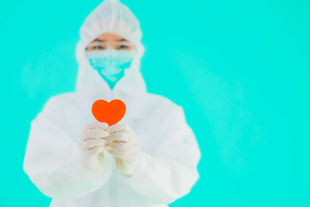 Portrait beautiful young asian doctor woman wear ppe or  personal protective equipment for protect from coronavirus or covid19 show heart on blue isolated background - Photo, Image