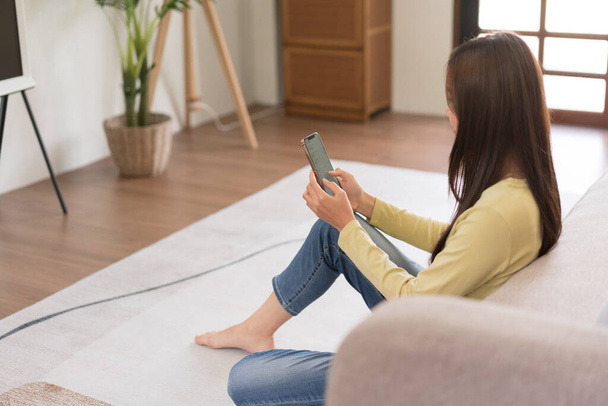 Vrijetijdsbesteding concept, Jonge vrouw te controleren online verkoopopbrengsten op de telefoon tijdens het zitten op de vloer. - Foto, afbeelding