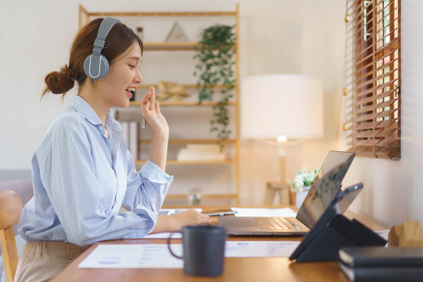 Remote business concept, Businesswoman wear headphone to meeting and greeting partner in video call. - 写真・画像