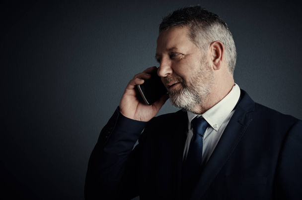 You have news for me. Studio shot of a handsome mature businessman looking thoughtful while making a call against a dark background - Photo, image