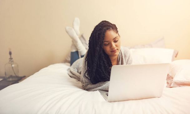 Интернет - это бездонная дыра в деятельности. молодая женщина использует ноутбук, лежа в своей спальне - Фото, изображение