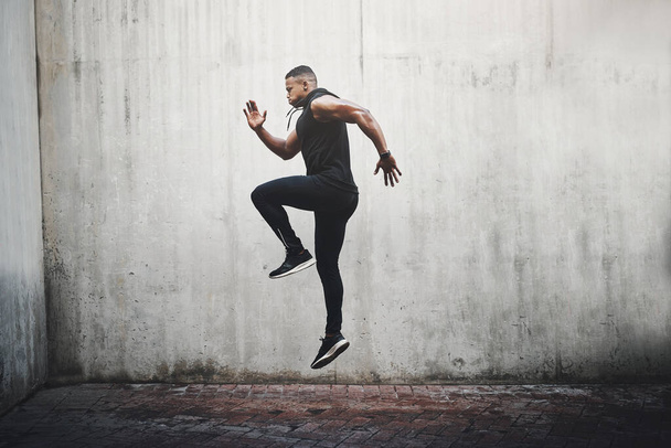 Jump, training and black man running, speed and energy for cardio fitness, workout and sports wellness or body health. Athlete, runner or person exercise on concrete wall, action run or moving in air. - Photo, Image