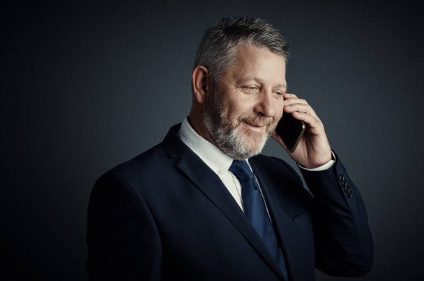 Great stuff. Studio shot of a handsome mature businessman looking thoughtful while making a call against a dark background - Foto, afbeelding