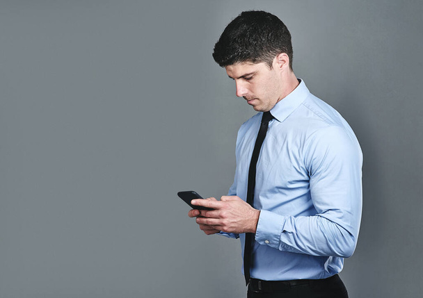Its essential to maintain communication with clients. Studio shot of a young businessman texting on a cellphone against a grey background - Foto, Imagen