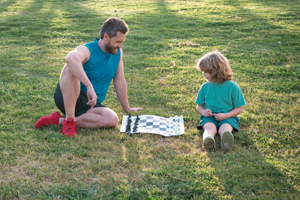 Отец и сын, маленький мальчик играет в шахматы, проводит время вместе на открытом воздухе в летнем парке - Фото, изображение