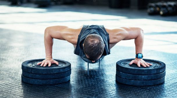 A legálisabb módja a fitt állapotnak. Egy fiatal férfi fekvőtámaszozik súlyokkal egy edzőteremben. - Fotó, kép