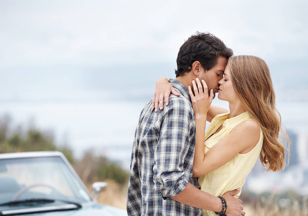 Roadside romance. An affectionate young couple standing alongside their convertible while on a roadtrip - Foto, imagen