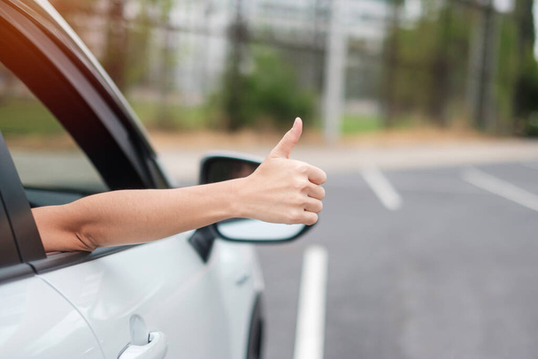 kobieta ręka kciuk w górę podczas jazdy samochodem na drodze, ręka sterująca kierownicą w elektrycznym nowoczesnym samochodzie. Koncepcje podróży, podróży i bezpieczeństwa Transport - Zdjęcie, obraz