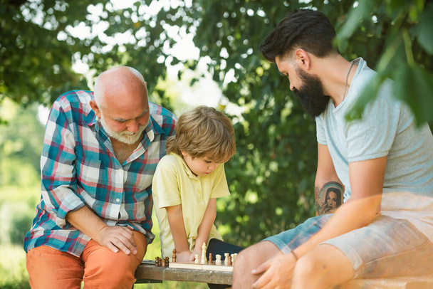 Happy loving family. Grandfather and grandson are playing chess and smiling while spending time together in park. Fathers day - Fotó, kép
