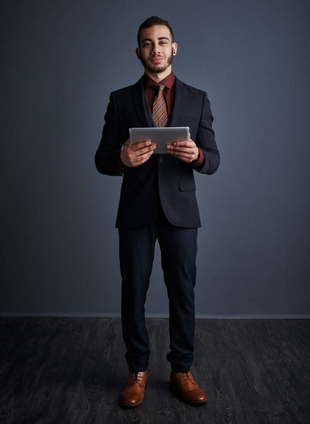 You have to look the part. Studio portrait of a stylish young businessman using a tablet against a gray background - Foto, afbeelding