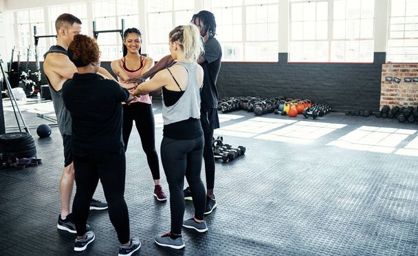 A fitneszről szól. egy vidám fiatal csoport, akik összebújnak, miközben az ember belenéz a kamerába edzés előtt egy edzőteremben. - Fotó, kép