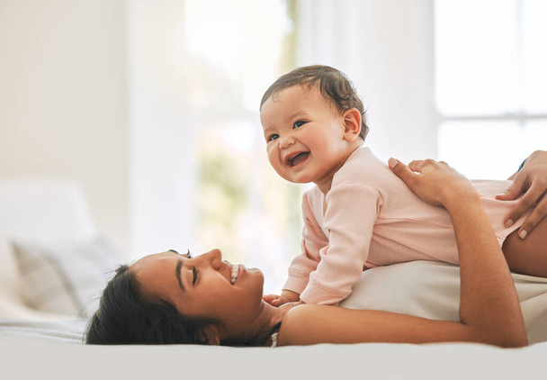 Mother lying, embrace newborn baby and bed with smile, care or happiness in morning with love, bond or excited face. Young mom, kid and happy in bedroom, family home or holding with pride in sunshine. - Photo, image