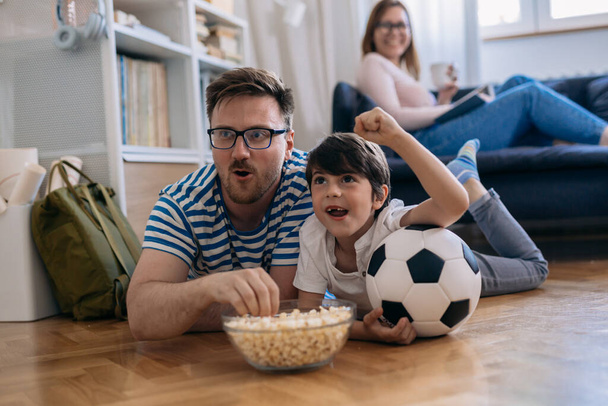 Caucasian family watches a soccer match together and cheers. - 写真・画像