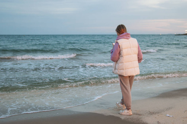 Портрет взволнованной девушки в руках с телефоном, стоящей на пляже с синим морем. Грустная и подавленная молодая женщина, стоящая одна на берегу моря. Концепция депрессии. Высокое качество фото - Фото, изображение