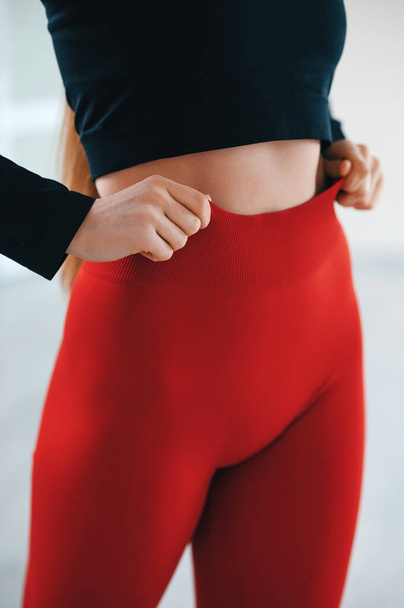 Close up view of female model posing at white studio background and demonstrating comfortable activewear. Front view of perfect fit body in slim black top and tight red leggings - 写真・画像