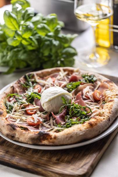 Round buffalo mozzarella on top of a ham, tmatoes and rocket pizza with crusty edges. - Foto, Imagem