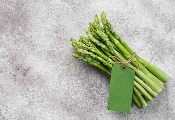 Fresh green asparagus with empty tag on grey concrete background. Flat lay - Foto, afbeelding