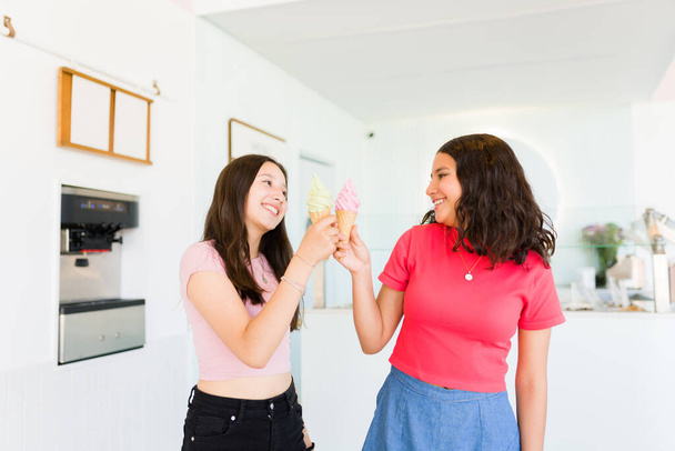 Best friends and teen girls laughing and looking cheerful while enjoying eating a delicious gelato cone at the ice cream shop - Fotografie, Obrázek