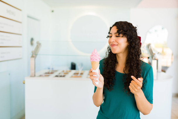 Латино приваблива молода жінка, яка їсть морозиво конус, виглядає щасливим, купивши заморожений йогурт в магазині.  - Фото, зображення
