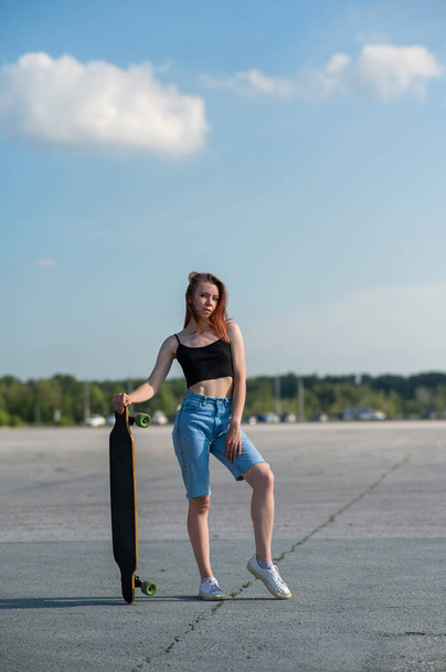 Young caucasian woman holding a long board outdoors - Foto, Bild
