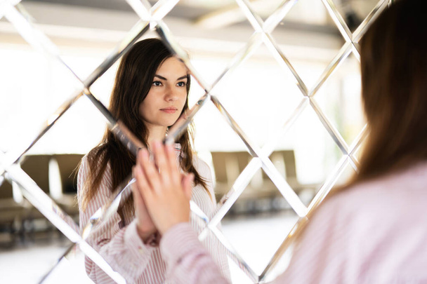 Young beautiful brunette woman in shirt touching mirror made of rhombuses.  - Zdjęcie, obraz