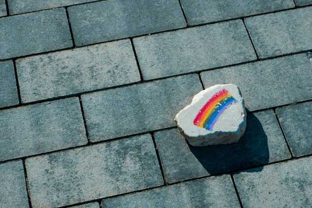 primer plano de una roca plana con una bandera de arco iris pintada en ella, en el pavimento de una calle - Foto, imagen