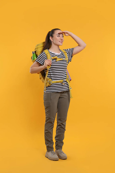 Smiling young woman with backpack on orange background. Active tourism - Valokuva, kuva