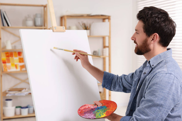 Man painting in studio. Using easel to hold canvas - 写真・画像