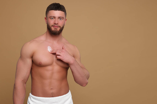 Handsome man applying body cream onto his chest on pale brown background, space for text - Fotó, kép