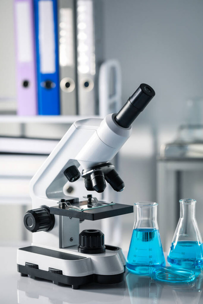 Different laboratory glassware with light blue liquid and microscope on table - Foto, immagini