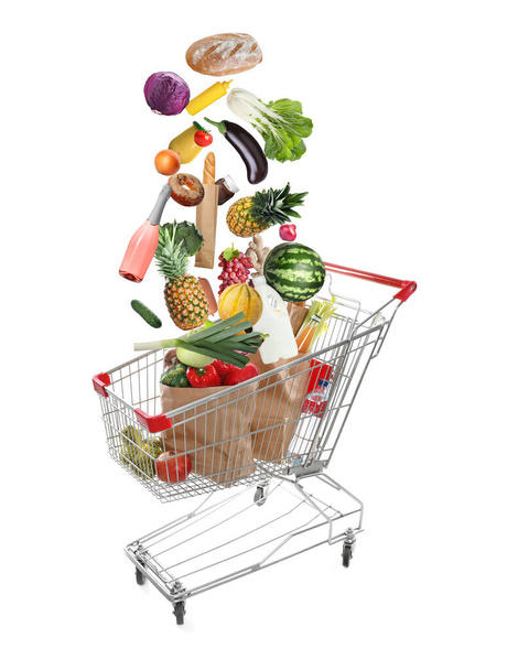 Market assortment. Different products falling into shopping cart on white background - Photo, Image