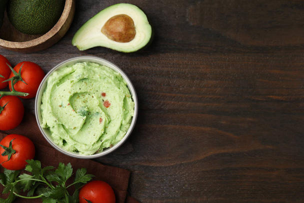 Bowl of delicious guacamole and ingredients on wooden table, flat lay. Space for text - Fotoğraf, Görsel