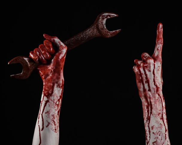 bloody hand holding a big wrench, bloody wrench, big key, bloody theme, halloween theme, crazy mechanic, murderer, psycho, violence, zombies, black background, isolated, revolution - Photo, image