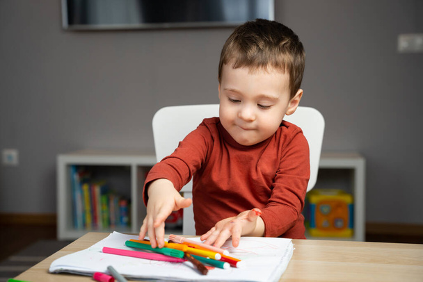 Roztomilý, šťastný dvouletý batole hrající si s markery na albu v dětském pokoji doma. Vzdělávací aktivity pro děti. Selektivní zaměření. - Fotografie, Obrázek