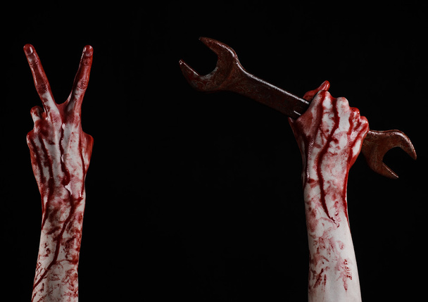 bloody hand holding a big wrench, bloody wrench, big key, bloody theme, halloween theme, crazy mechanic, murderer, psycho, violence, zombies, black background, isolated, revolution - Foto, Bild
