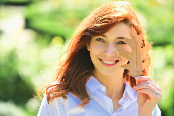 Cheerful smiling ginger woman holding fall oak leaves. Healthy and natural woman beauty. Happy smiling girl with natural red hair. Autumn woman with bright orange hair - Photo, Image