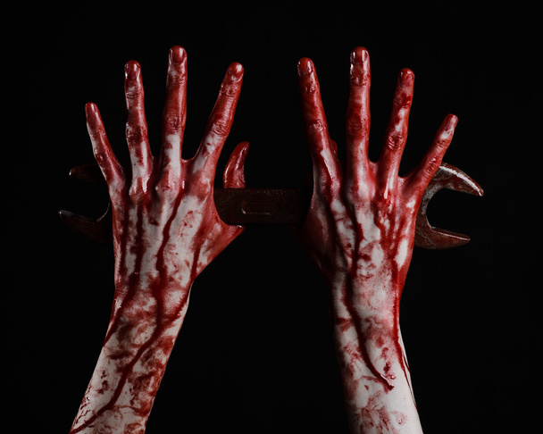 bloody hand holding a big wrench, bloody wrench, big key, bloody theme, halloween theme, crazy mechanic, murderer, psycho, violence, zombies, black background, isolated, revolution - Photo, Image