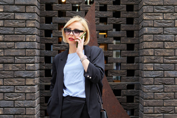 Una donna d'affari che cammina dall'altra parte della strada parlando con uno smartphone. Felice sorridente caucasico occupato donna d'affari. - Foto, immagini