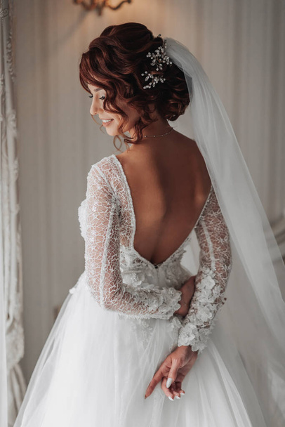 Red-haired bride in a beautiful dress, model posing, photo from the back, dress with a slit on the back. Wedding. wedding bouquet Morning of the bride. A happy bride is waiting for the groom. - Fotó, kép