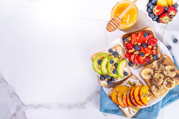 Fruit berry sandwiches. Various toasts with peanut butter, cream cheese, chocolate spread with summer berries and fruits - strawberry, banana, peach, apple, blueberry, Tasty morning lunch food - Photo, Image