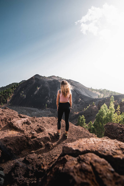 Woman with long hair marveling at the volcanic landscape of the Cumbre Vieja lava mountains at sunset, during her adventure on the Canary Island of La Palma - 写真・画像