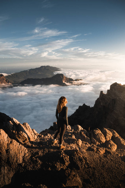 Young woman enjoying a beautiful sunset from the top of Roque De Los Muchachos with a sea of clouds over Caldera De Taburiente on the Canary Island of La Palma. - Fotoğraf, Görsel