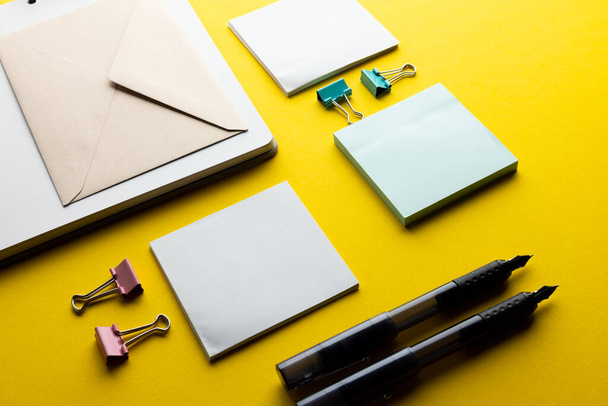 Flat lay of black pens, envelope and white paper with copy space on yellow background. School materials, writing, colouring, drawing, learning, school and education concept. - 写真・画像
