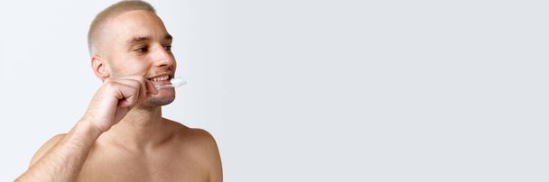 Young shirtless man taking care after teeth, brushing against white studio background. Concept of mens beauty, skincare, dental teeth care, health. Copy space for ad. Banner - Foto, Imagen