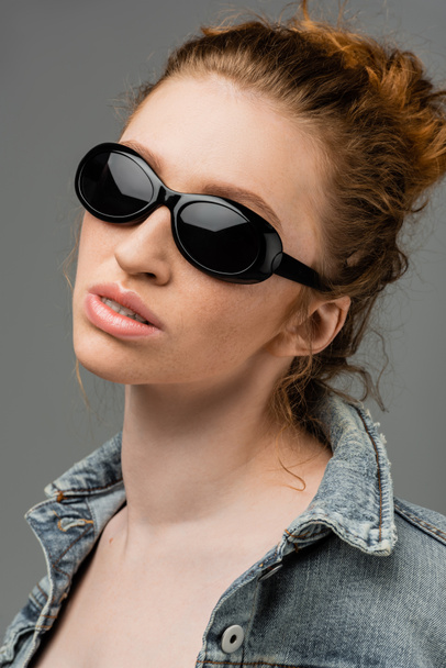 Retrato de jovem ruiva e mulher sardenta em óculos de sol na moda e jaqueta de ganga de pé isolado em fundo cinza, conceito de proteção solar na moda, modelo de moda  - Foto, Imagem