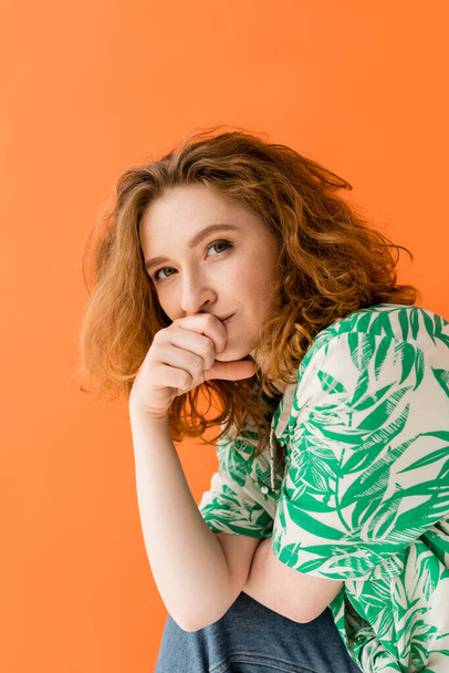 Portrait of young redhead woman with no-makeup look wearing modern blouse with floral print and jeans while looking at camera isolated on orange, trendy casual summer outfit concept, Youth Culture - Photo, image