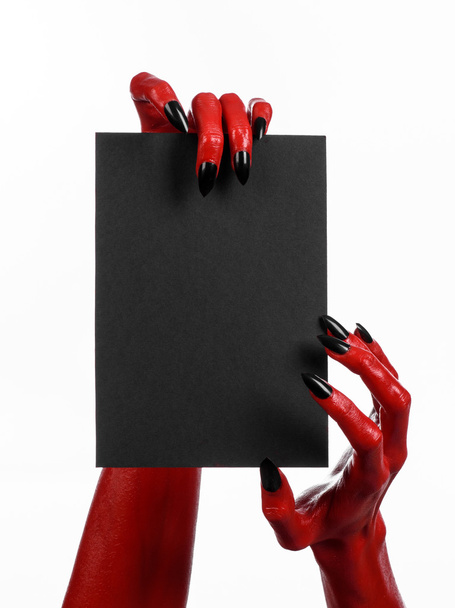 Halloween theme: Red devil hand with black nails holding a blank black card on a white background - Foto, Bild